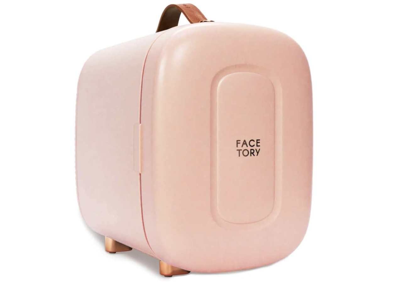A blush pink FaceTory mini skincare fridge with a curved design, gold-toned legs, and a leather handle for portable use.