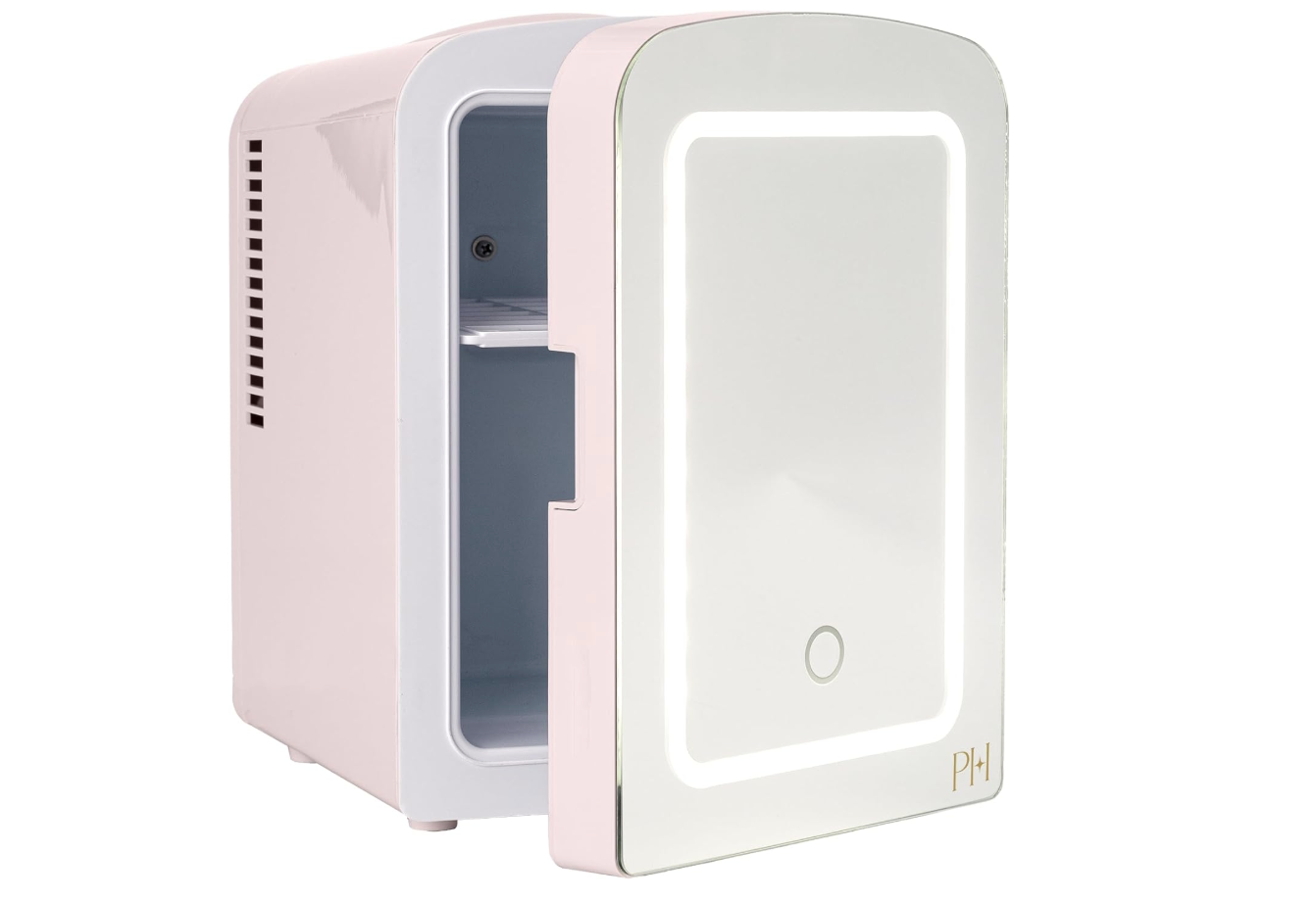 A pastel pink mini fridge with a glossy LED mirror door, partially open to reveal an empty interior and featuring a small PH logo in gold.