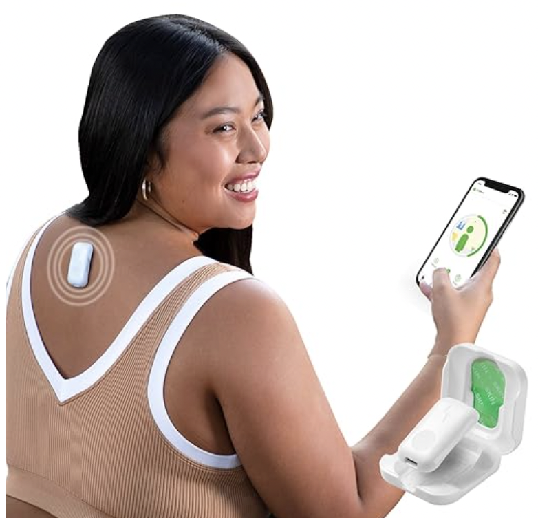 A woman smiles while using a smart posture tracker attached to her upper back, connected to a mobile app displayed on her phone, with the device case shown in the corner.