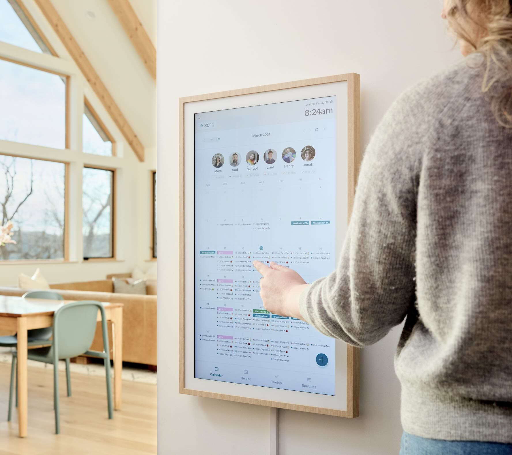 An adult uses the Hearth Display touchscreen in a sunlit home to manage a shared digital calendar for the whole family.